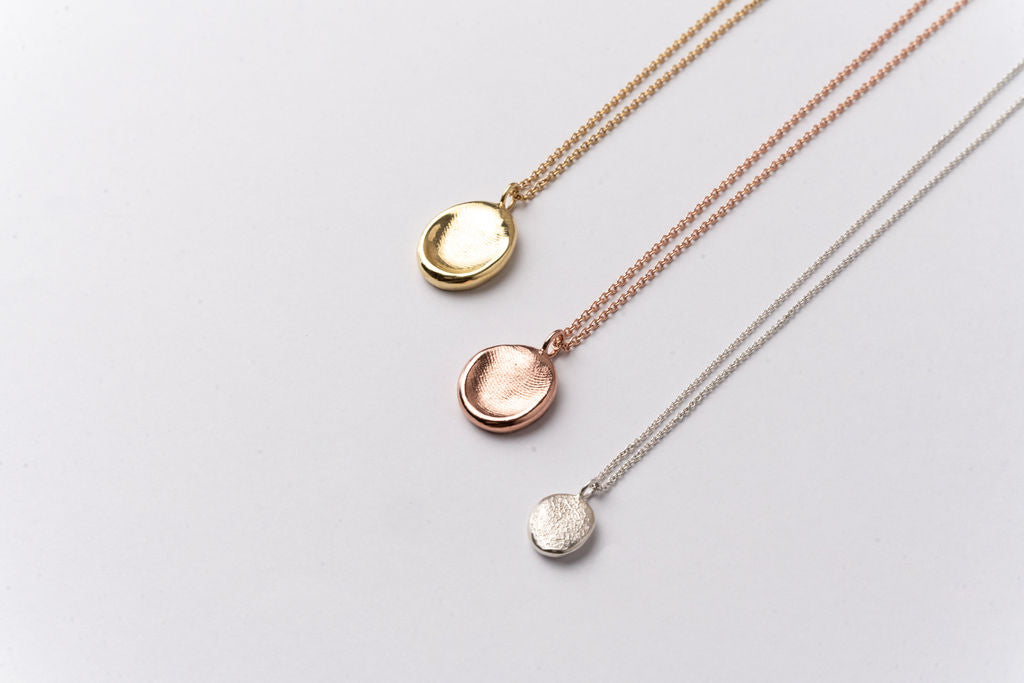 Three impression pendants on chains, in yellow gold, rose gold and silver, displayed on a clean white background.