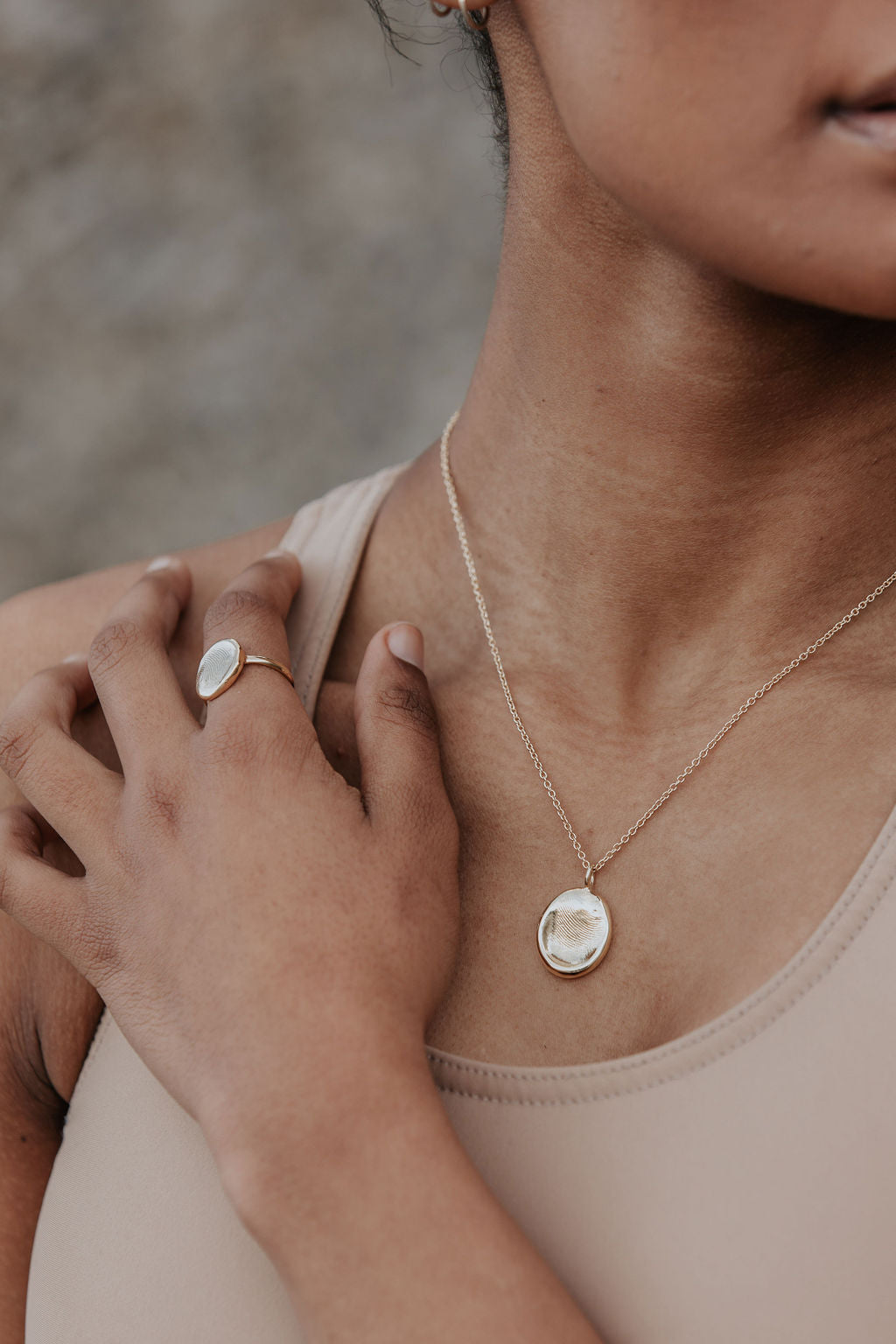 A close up of a lady wearing a fingerprint impression necklace and ring. 