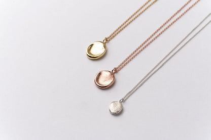 Three impression pendants on chains, in yellow gold, rose gold and silver, displayed on a clean white background. 