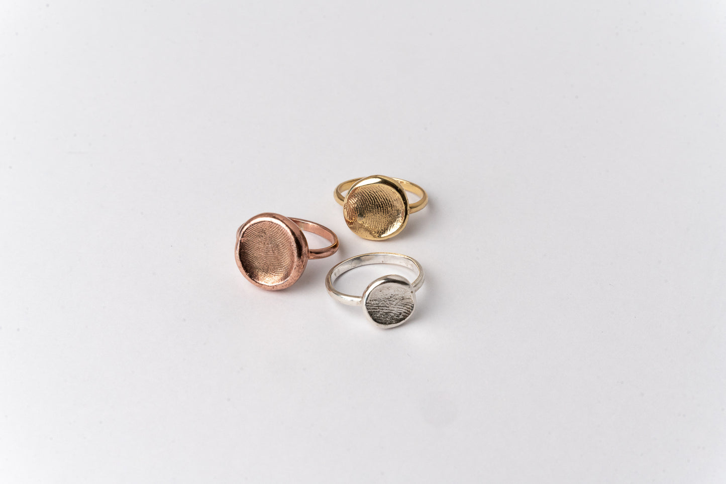 Three ROHO Heritage Jewellery fingerprint impression rings in silver, yellow gold and rose gold, displayed on a clean white background.