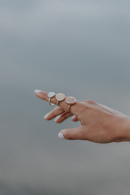 An artistic photo of a lady's hand with three impression rings displayed on her finger, in silver, yellow gold and rose gold. 