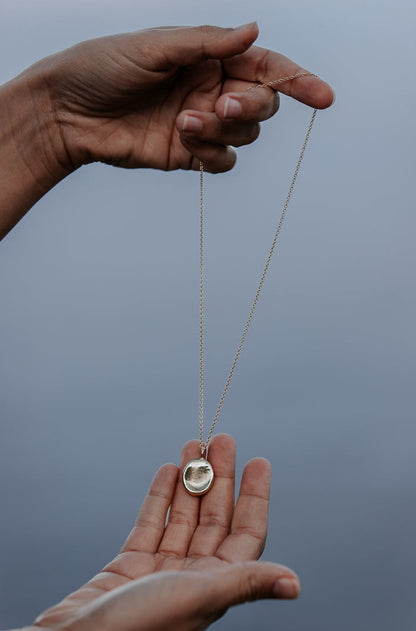 An elegant image of two hands holding a gold fingerprint impression pendant on a chain.